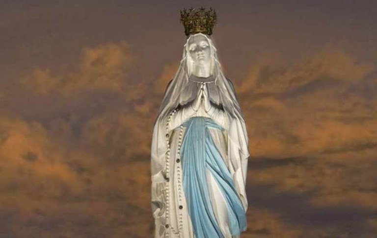 Statue couronnée de Notre-Dame de Lourdes sur fond de ciel au crépuscule