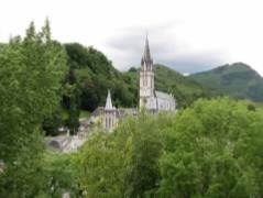 Vue sur les basiliques de Lourdes entre les arbres, au pied des montagnes