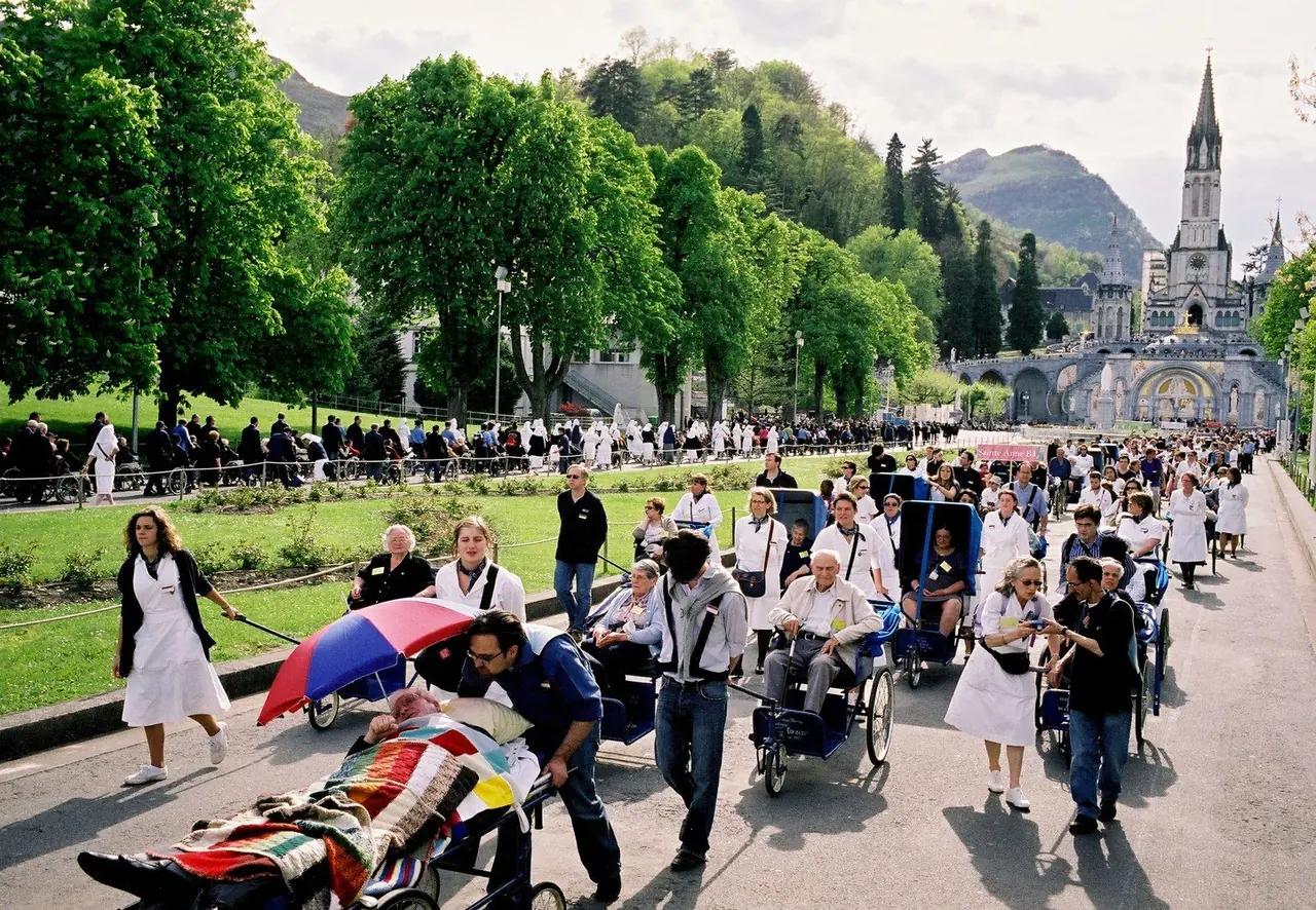 Des hospitaliers de l’A.B.I.I.F. accompagnent les pèlerins en voiturette vers la basilique de Lourdes