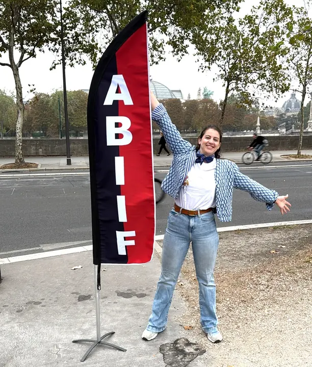 Une hospitalière à côté de l’oriflamme de l’A.B.I.I.F.